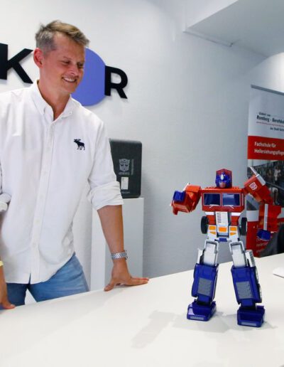 Mann steht neben einem Optimus Prime Roboter, der auf einem Tisch platziert ist.